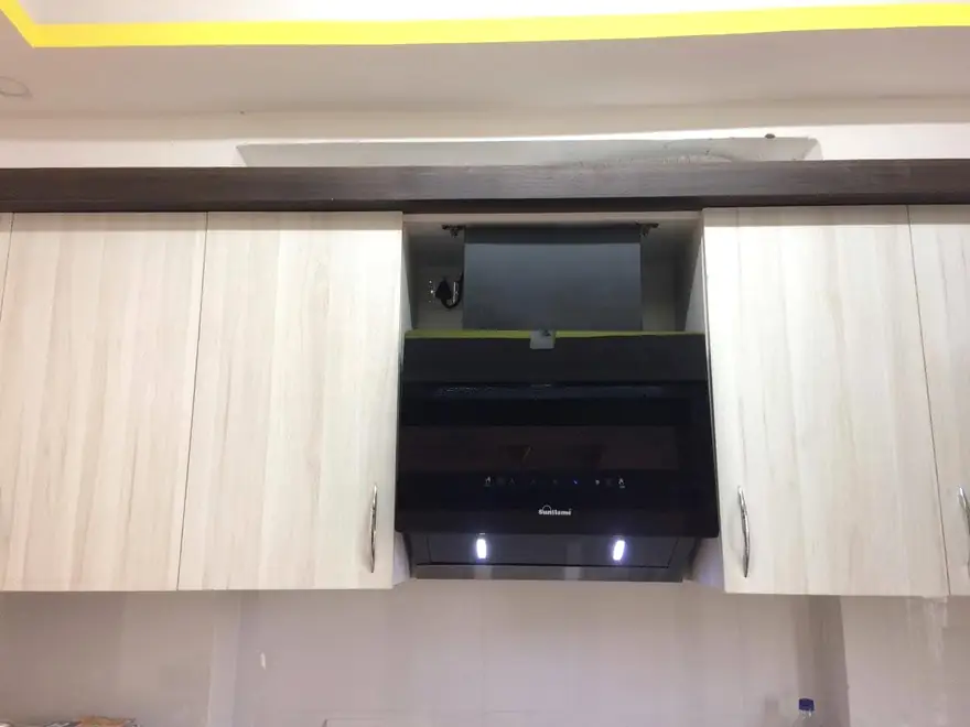 Angled chimney fitted between light wood wall cabinets